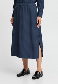 Jupe midi bleu marine avec des rayures verticales, taille élastique et fentes latérales. Porte avec des mocassins noirs brillants. Texture lisse.