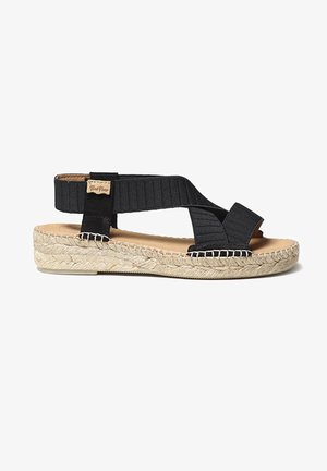 Sandales espadrilles noires avec des brides croisées élastiques, semelle en jute et empeigne texturée. Présente une petite étiquette de marque sur le côté.