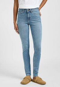 Jeans skinny de mezclilla azul con cintura alta, que cuentan con cinco bolsillos y un cierre de cremallera con botón. Textura suave y sin adornos visibles.