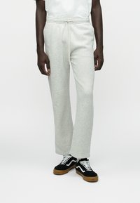 Pantalones de chándal de mezcla de algodón gris claro con cintura ajustable. Corte holgado, piernas rectas y textura notable. Llevados con zapatillas negras y blancas.