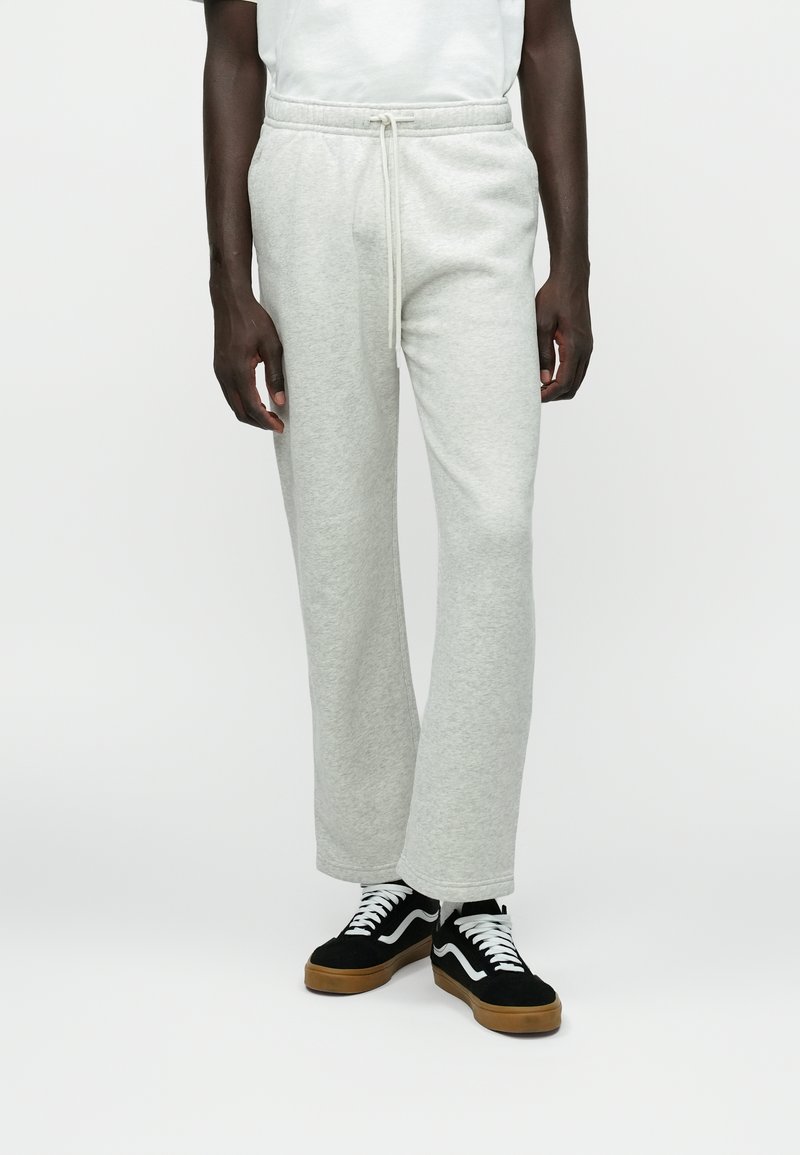 Pantalones de chándal de mezcla de algodón gris claro con cintura ajustable. Corte holgado, piernas rectas y textura notable. Llevados con zapatillas negras y blancas.