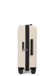 Valigia rigida beige, con strisce verticali testurizzate, zip nera, lucchetto TSA e quattro ruote per una facile mobilità.