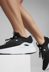 Svarta och ljusblå atletiska skor med ovandel i mesh, tjock vit sula och intrikat sömnad. Snören och detaljer i metalldelar är närvarande.