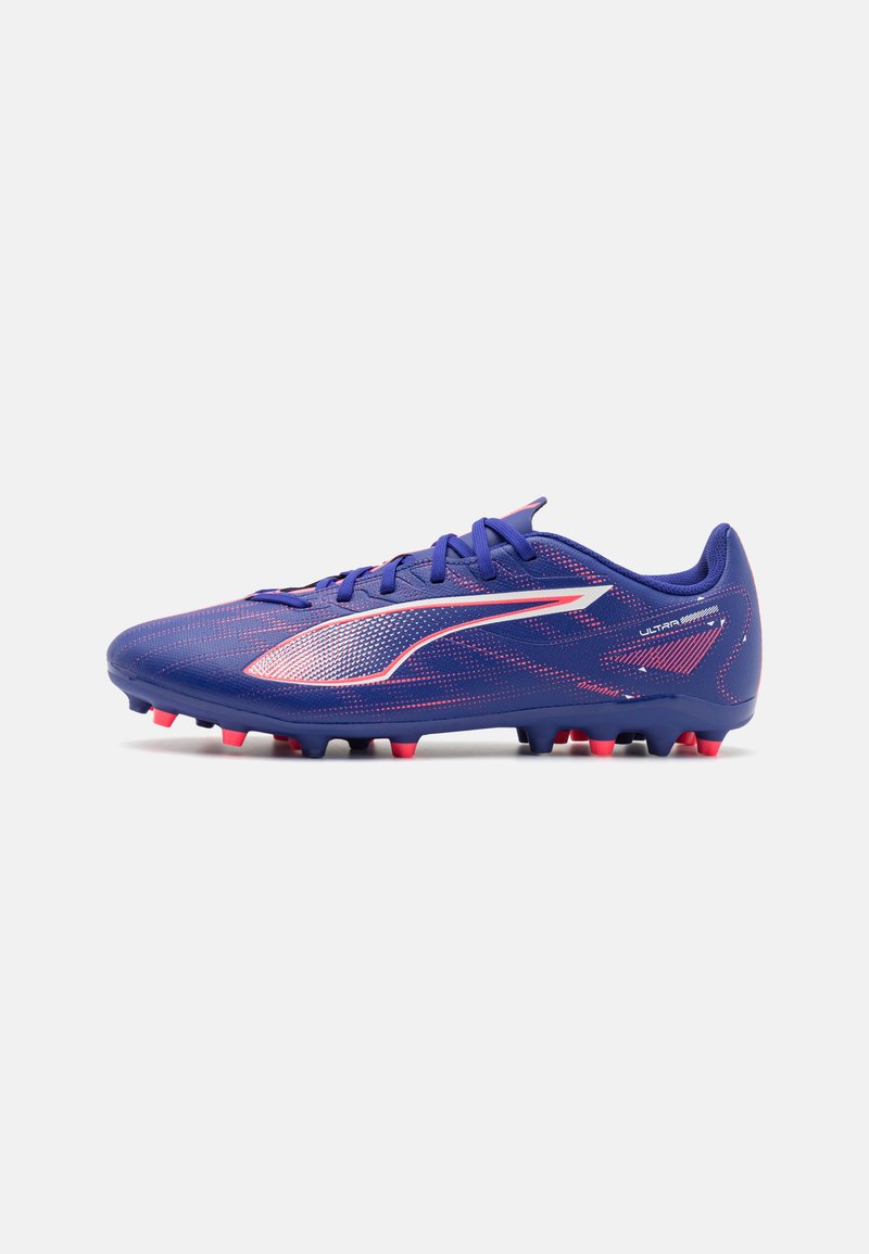 Botín de fútbol morado con una superficie texturizada, detalles en blanco y tachuelas rojas. Presenta un perfil bajo y un diseño con cordones.