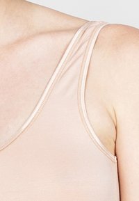 Helles rosa Tanktop mit d ünnen Trägern, weicher Textur und glatter Oberfläche. Verfügt über einen abgerundeten Ausschnitt und saubere Nähte entlang der Kanten.