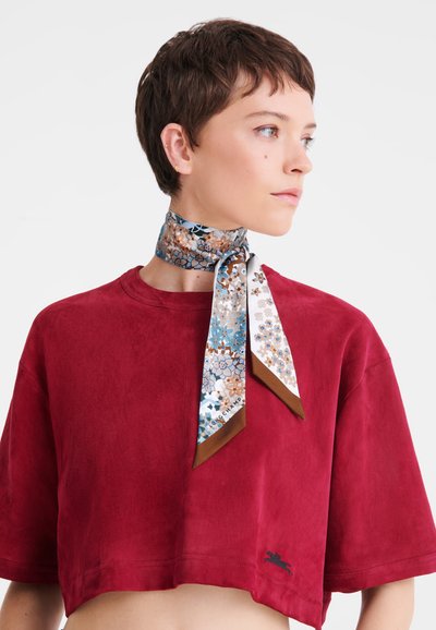 Silk scarf with a blue, brown, and white floral pattern; finished with angled brown edges. Worn around the neck over a red cropped top.