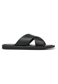 Sandales plates noires avec un design à lanières croisées en matériau lisse, une semelle extérieure texturée et des détails minimalistes.