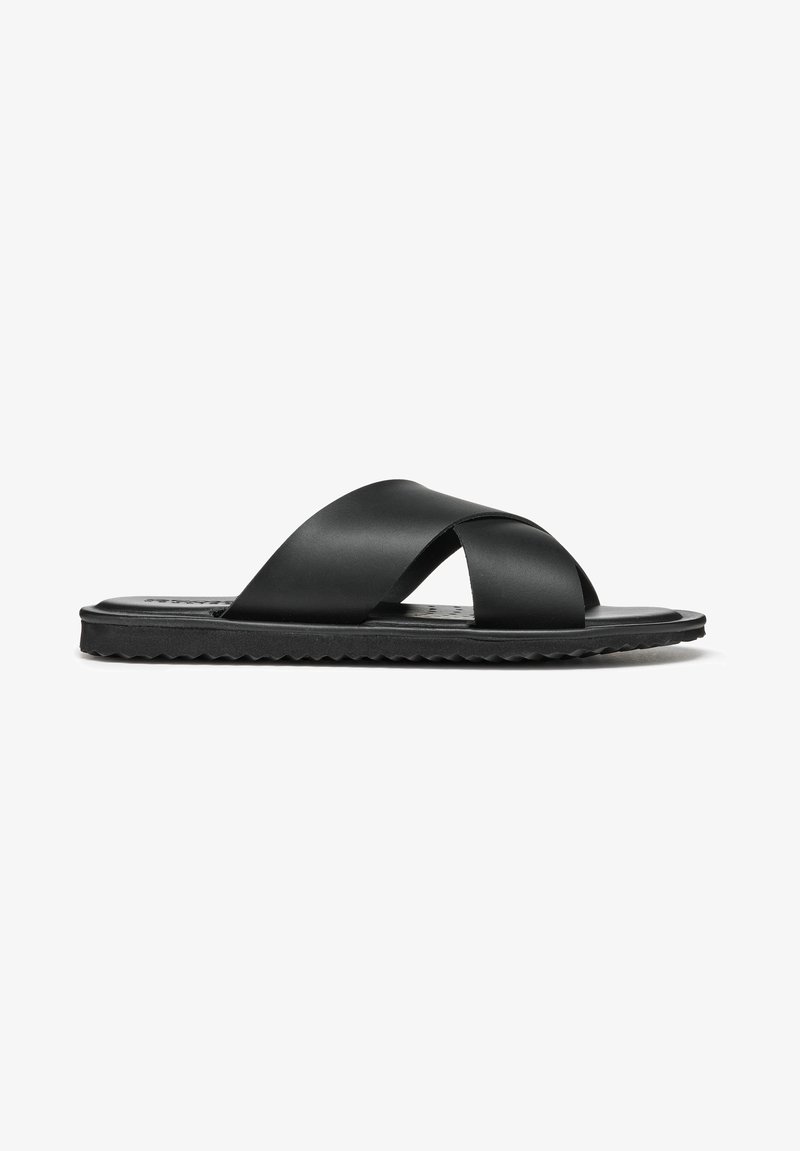 Svarta platta sandaler med ett korsremdesign som är gjorda av mjukt material, med en strukturerad yttersula och minimalistiska detaljer.