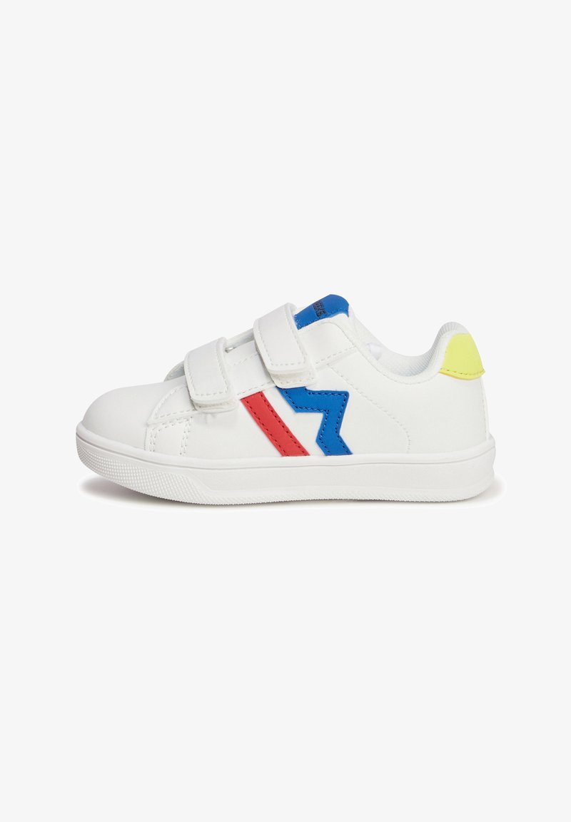 Baskets blanches avec des bandes Velcro, ornées d'accents en zigzag bleu et rouge et d'une languette de talon jaune, en matériau synthétique.