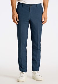 Skräddarsydda marinblå byxor i en mjuk tyg, med platt front, bälteshällor och knäppning fram, kombinerade med vita sneakers.