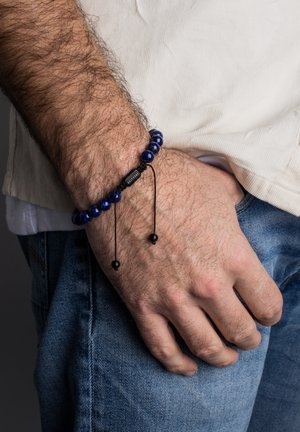 Mėlyna karoliukų apyrankė su juodu reguliuojamu virve ir karoliukais. Sukurta iš lygių, apvalių lapis lazuli akmenų, su mažu juodu stačiakampiu akcentu.