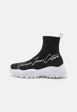 Sort sokkestil sneakers med hvid chunky sål og "Versace Jeans Couture" tekst i kursiv på siden.