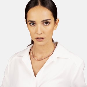 Collar de cuentas rosa con piedras redondas, usado sobre una camisa blanca con cuello. Las cuentas varían en tamaño y crean una textura sutil.