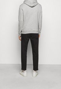 Sudadera con capucha gris, pantalones negros y zapatillas blancas. La sudadera tiene un dobladillo y puños acanalados, mientras que los pantalones son de corte recto.