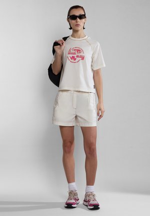 Geknipte crèmekleurige t-shirt met een rode graphic en bijpassende crèmekleurige shorts. Lichtgewicht stof, ontspannen pasvorm, en gedragen met roze en beige sneakers.