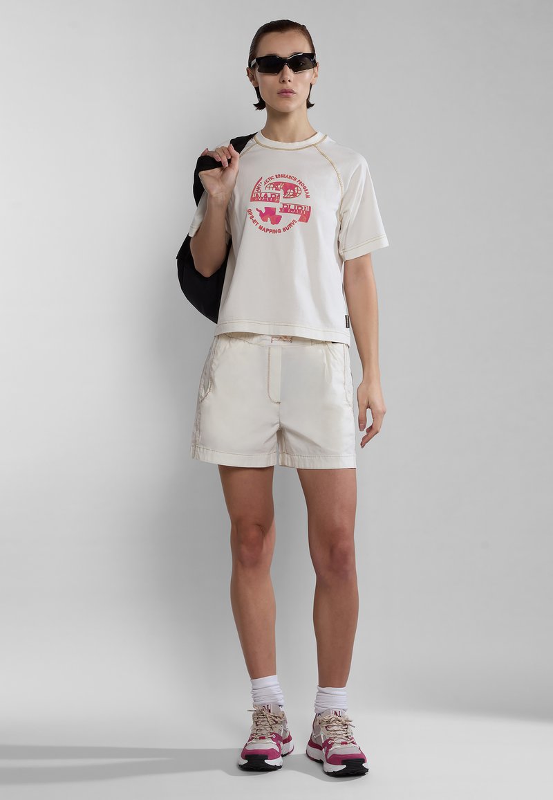 Gekürztes cremefarbenes T-Shirt mit rographic und passenden cremefarbenen Shorts. Leichter Stoff, lockere Passform und kombiniert mit pinken und beigen Sneakers.