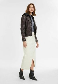 Braune Leder-Bikerjacke mit Reißverschluss, langer cremefarbener Rock mit vorderem Schlitz und schwarze, mit Reptilstruktur versehene, blockierte Absatzstiefel.