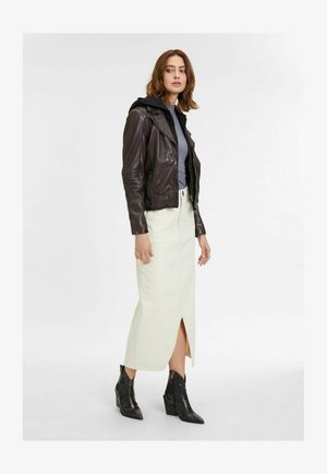 Giacca di pelle marrone con cappuccio nero, maglia grigia, gonna midi color crema con spacco frontale e stivaletti neri con tacco e finitura testurizzata.