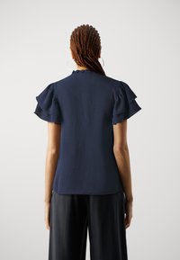 Blusa blu navy con maniche corte a volant e una finitura leggermente strutturata. Presenta un colletto alto e una vestibilità comoda.