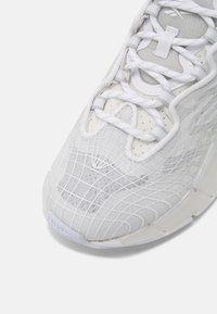 Vit atletisk sko framifrån med strukturerad meshöverdel, vita snören och vadderad tunga på vit bakgrund.