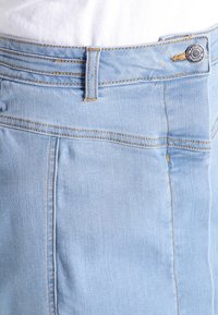 Vaaleansininen farkkuhame, jossa on kapea malli, näkyvät ompeleet, etupainike ja viiden taskun malli. Pehmeä rakenne.