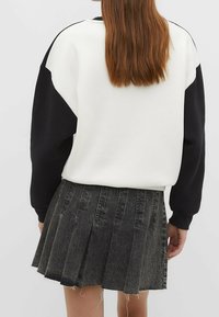 Sweatshirt van een katoenmix met zwarte mouwen en een wit lijf, gecombineerd met een zwarte, geplooide denimrok met een rafelige zoom.