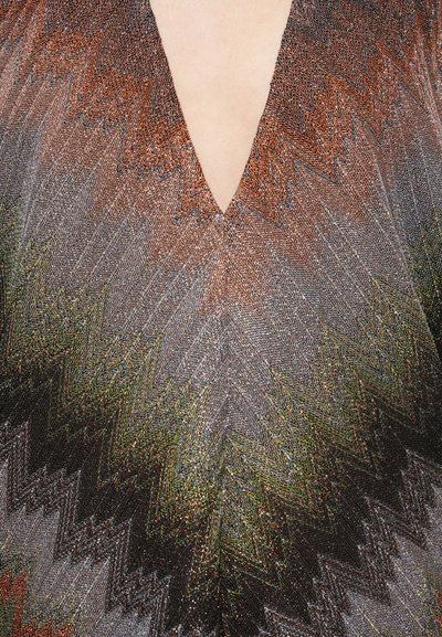 Pletený odev s hlbokým výstrihom do V, zdobený cikcak vzorom v prírodných odtieňoch hnedej, zelenej a sivej s kovovými akcentmi.