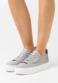 Sneakers in pelle grigia con suola in gomma bianca, punta tonda e lacci grigi. Presentano una texture liscia e un design minimalista.