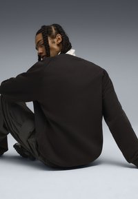 Felpa nera con collo a giro dal taglio relaxed, caratterizzata da maniche lunghe e una texture liscia, indossata sopra pantaloni cargo scuri.