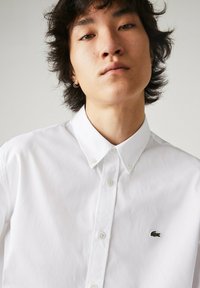 Witte button-up shirt van katoen, met een klassieke kraag, groen geborduurd logo op de linkerborst en een gladde textuur.