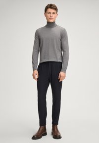 Szary sweter golfowy w zestawieniu z ciemnymi spodniami i brązowymi botkami do kostek. Sweter ma gładką strukturę i dopasowany krój.