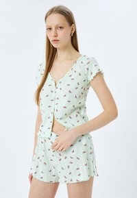 Hellgrünes Schlafanzug-Set mit einem kurzärmeligen Oberteil und passenden Shorts im Wassermelonen-Kern-Muster. Knopfverschluss und geraffte Kanten.