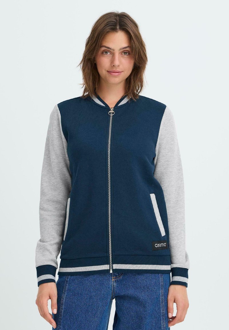 Tumesinine ja hall zip-up bomber-jakk, ribidega krae ja varrukaotsad, küljetaskud, pehme kangas, brändi logo silt hemme juures.