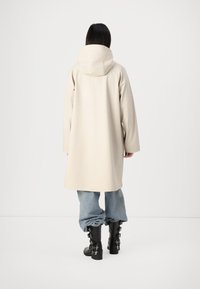 Beige oversized jacka med huva och långa ärmar, tillsammans med ljusblå baggy jeans och svarta knähöga stövlar med sidspännen.