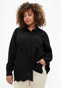 Camicia nera con bottoni e maniche lunghe, caratterizzata da un tessuto strutturato e un orlo a scallop con ricamo ad occhio e ritagli circolari.