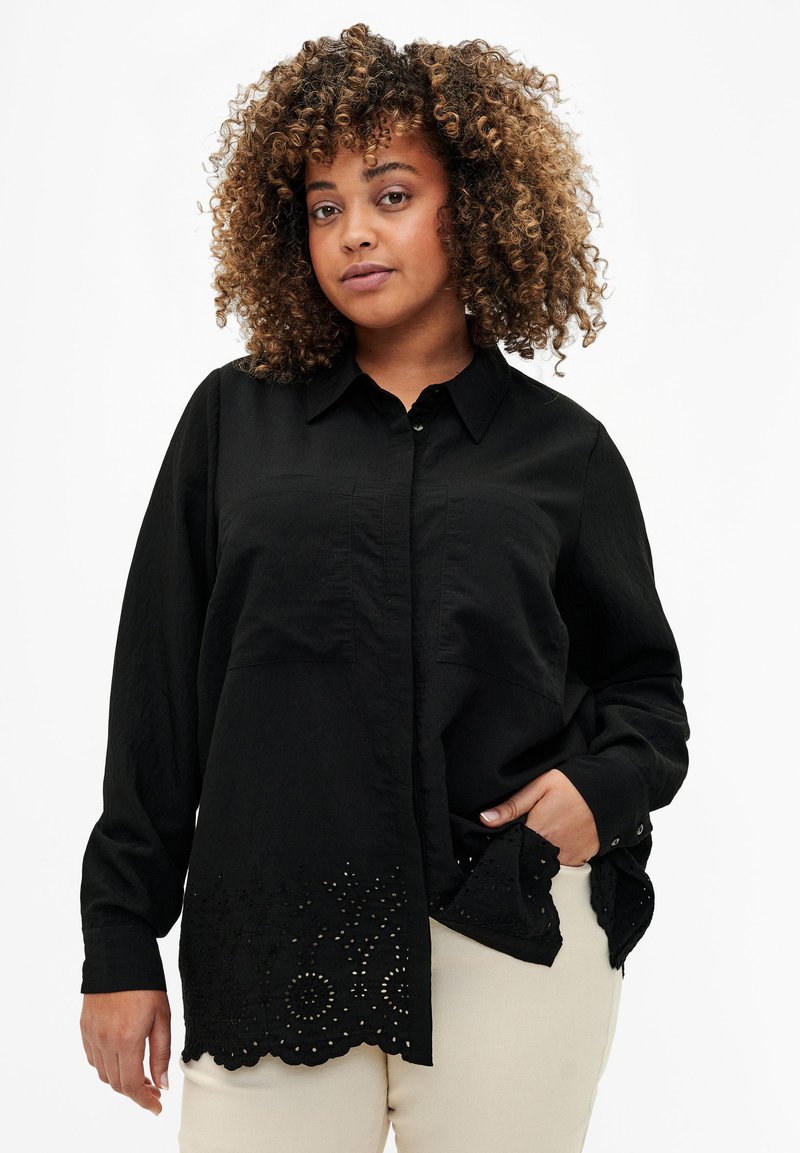 Camicia nera con bottoni e maniche lunghe, caratterizzata da un tessuto strutturato e un orlo a scallop con ricamo ad occhio e ritagli circolari.