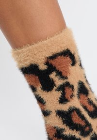 Calcetín peludo con estampado de leopardo que presenta tonos de marrón y negro en una tela suave y texturizada, con un puño que tiene un acabado esponjoso.