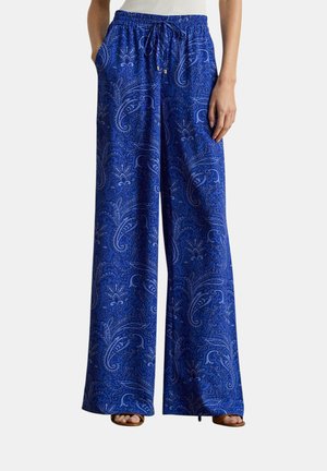 Pantaloni larghi blu con elastico in vita e coulisse, con un intricato motivo paisley, indossati con sandali aperti.