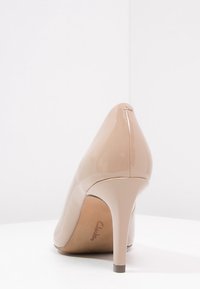 Nude lakierowane buty na wysokim obcasie z wąskim noskiem i smukłym obcasem typu stiletto, o gładkim, błyszczącym wykończeniu.