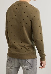 Maglione verde oliva con piccoli motivi a quadrati neri, polsini e orlo a coste, scollo rotondo e tessuto strutturato. Vista posteriore mostrata.