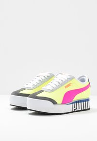 Tenisky Puma s neónovým žlutým a růžovým designem, šedými semišovými akcenty, bílými tkaničkami a robustní bílou podrážkou s grafickými detaily.