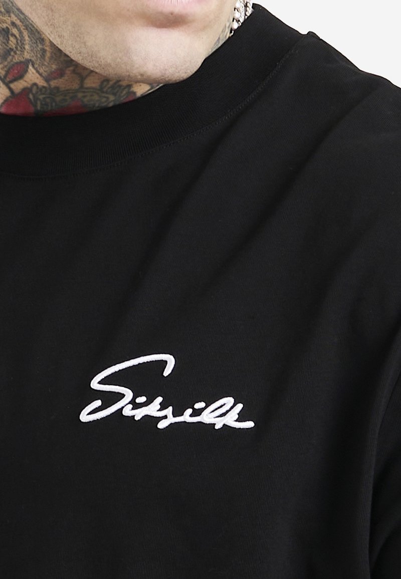 T-shirt en coton noir avec un logo "Sissilk" blanc brodé sur la poitrine gauche, col rond et manches courtes.