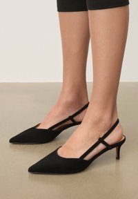 Escarpins slingback en daim noir avec un bout pointu, une bride à la cheville et un talon haut et fin. Texture lisse avec peu de détails.