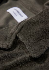 Ciemnoszary, teksturowany materiał o miękkiej, puszystej powierzchni. Posiada kołnierz z etykietą „UNIQUE 21” wszytą w materiał.