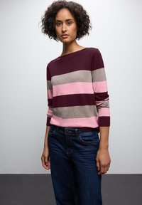 Gestreepte trui in maroon, grijs en roze, met lange mouwen en een bootnekkraag. Gecombineerd met donkerblauwe jeans in een relaxte pasvorm.