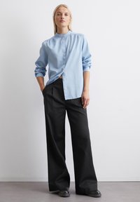 Light blue button-up shirt with a high collar and rolled sleeves, paired with loose black trousers and black shoes; minimalistic design.