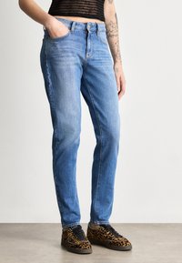 Jeans din denim albastru deschis, cu croială dreaptă, cinci buzunare și ușoare decolorări. Asortați cu adidași cu imprimeu de leopard în nuanțe de negru și maro.