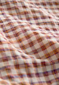 Baumwollstoff mit karierter Musterung in Orange, Lila und Blau. Weiche Textur mit sichtbarem Gewebe, das leichte Wellen im Material offenbart.