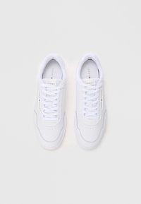 Zapatillas deportivas blancas con una superficie de cuero suave, cordones planos, puntera perforada y detalles de logo en el lateral.
