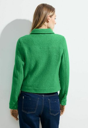 Veste en polaire verte avec un col structuré, des manches longues et un design court, présentant une texture douce et des coutures détaillées.